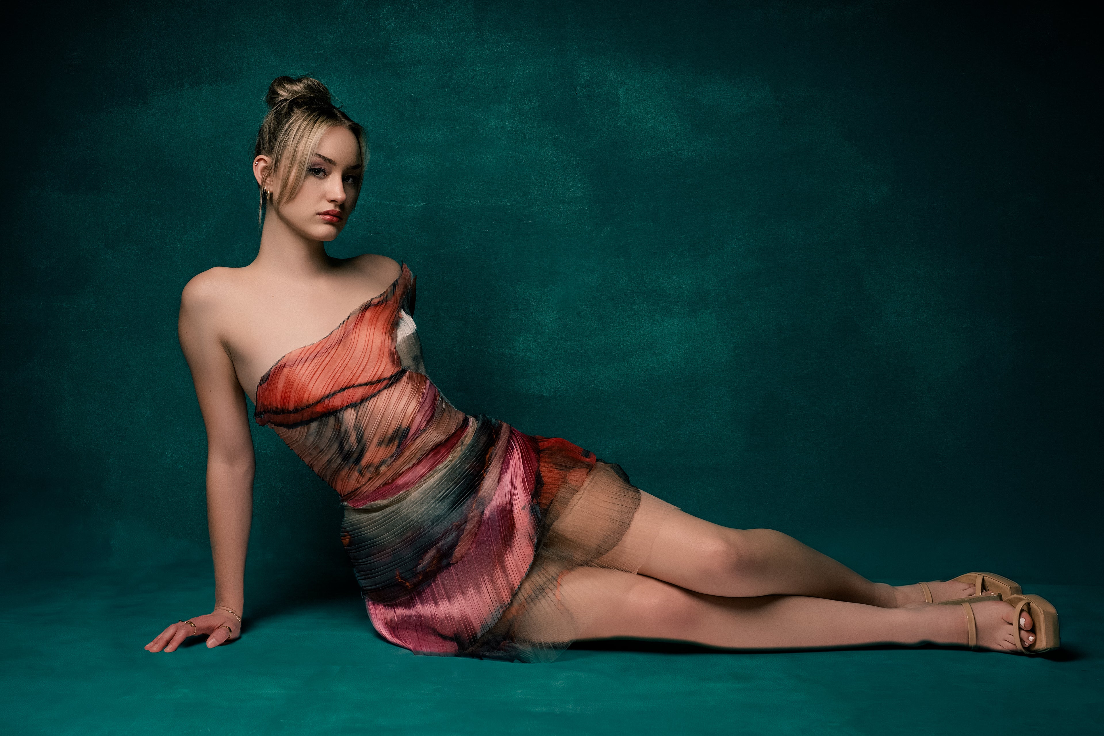 Woman in a colorful dress sitting on a teal background